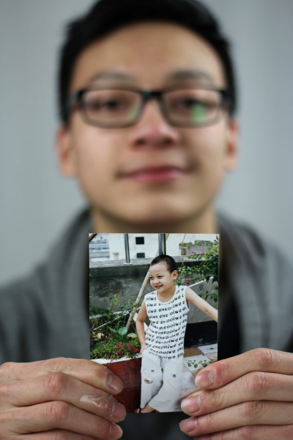 Zheng is photographed holding a childhood picture of himself during his time in China. Photo Credit / Christian Baker