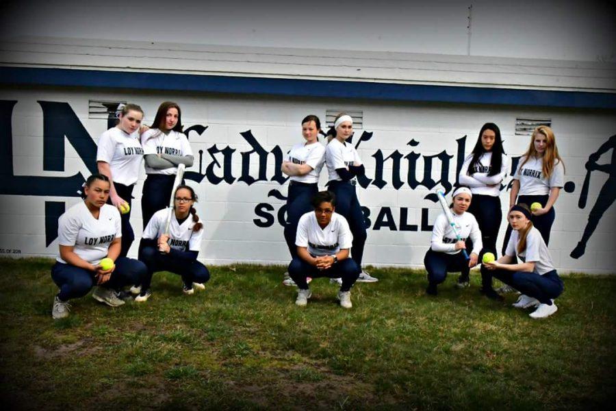 The varsity womens softball team pose for a picture in front of the dug-out. Photo Credit / Kristi Johnson