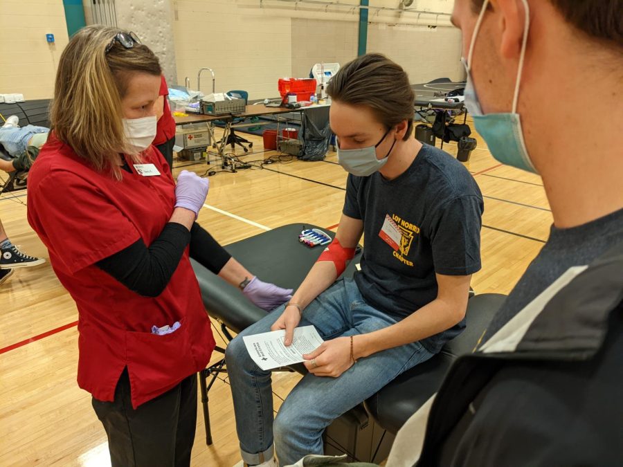 Senior Liam Braun is given instructions by a Red Cross staff member after donating blood. Loy Norrix students had the opportunity to donate blood on March 21 in the auxiliary gym.