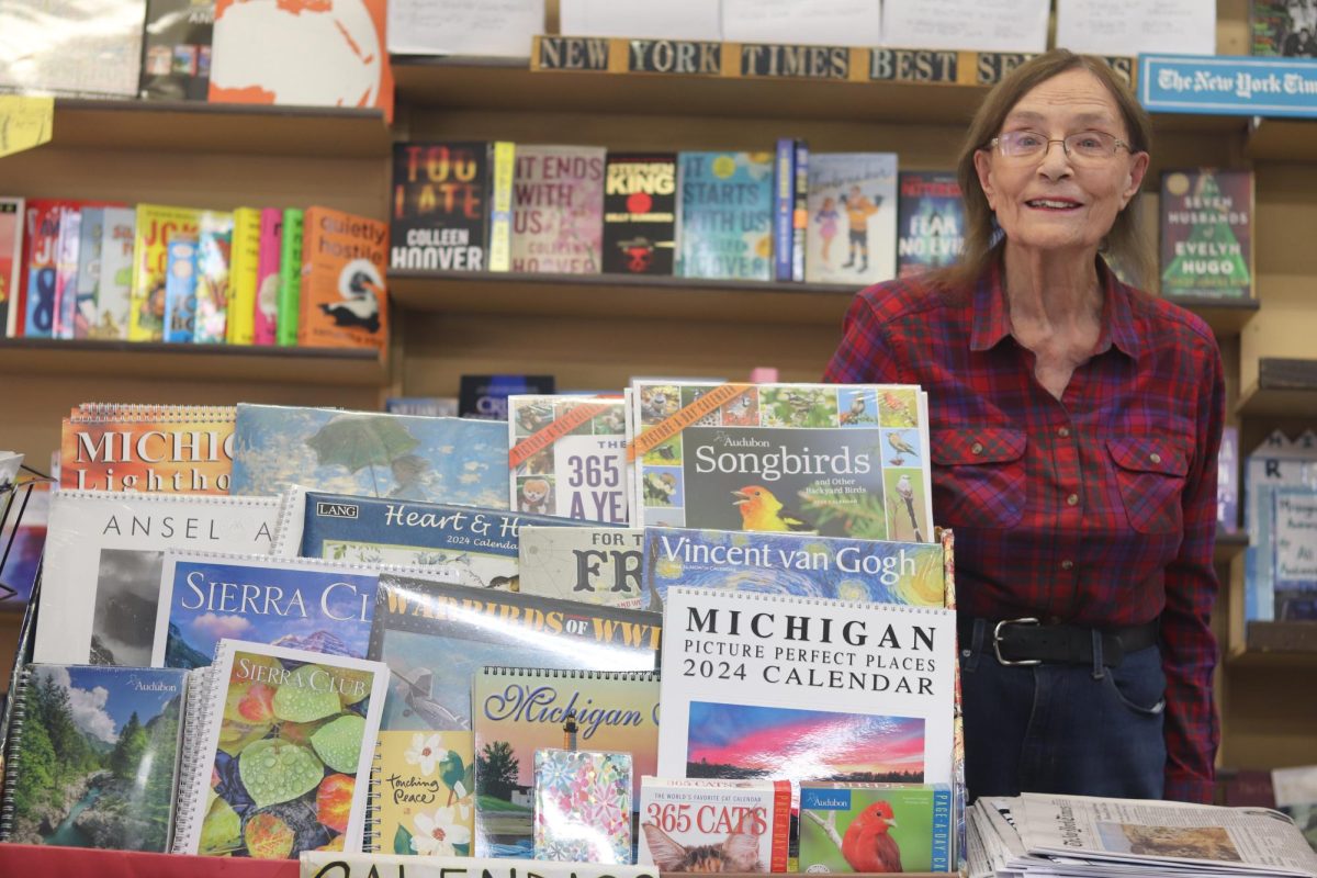 Dean Hauck is posing at the entrance of Michigan News Agency. She is standing next to the new calendars for the 2024 year.
