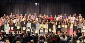 New and old NHS members gather on the stage after the ceremony. Proud friends and family take photos of the inductees. 