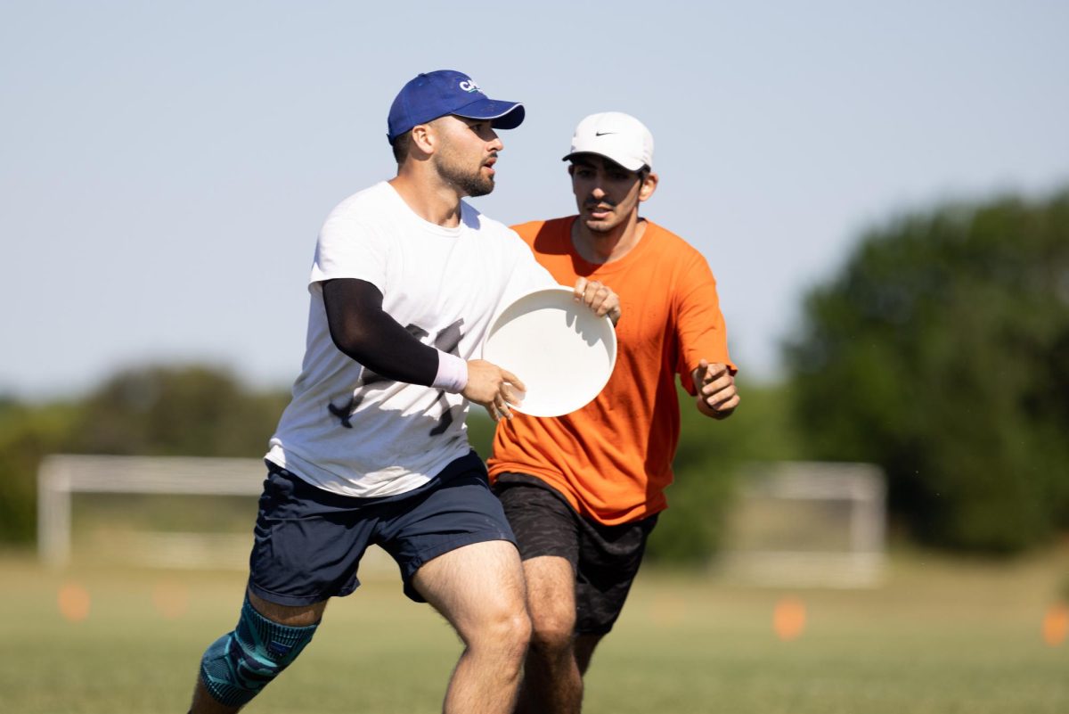 Latin and geometry teacher Dyami Hernandez plays ultimate frisbee on a local soccer field. He wears a white jersey as he plays for the Kalamazoo Ultimate Disc League club team. 
