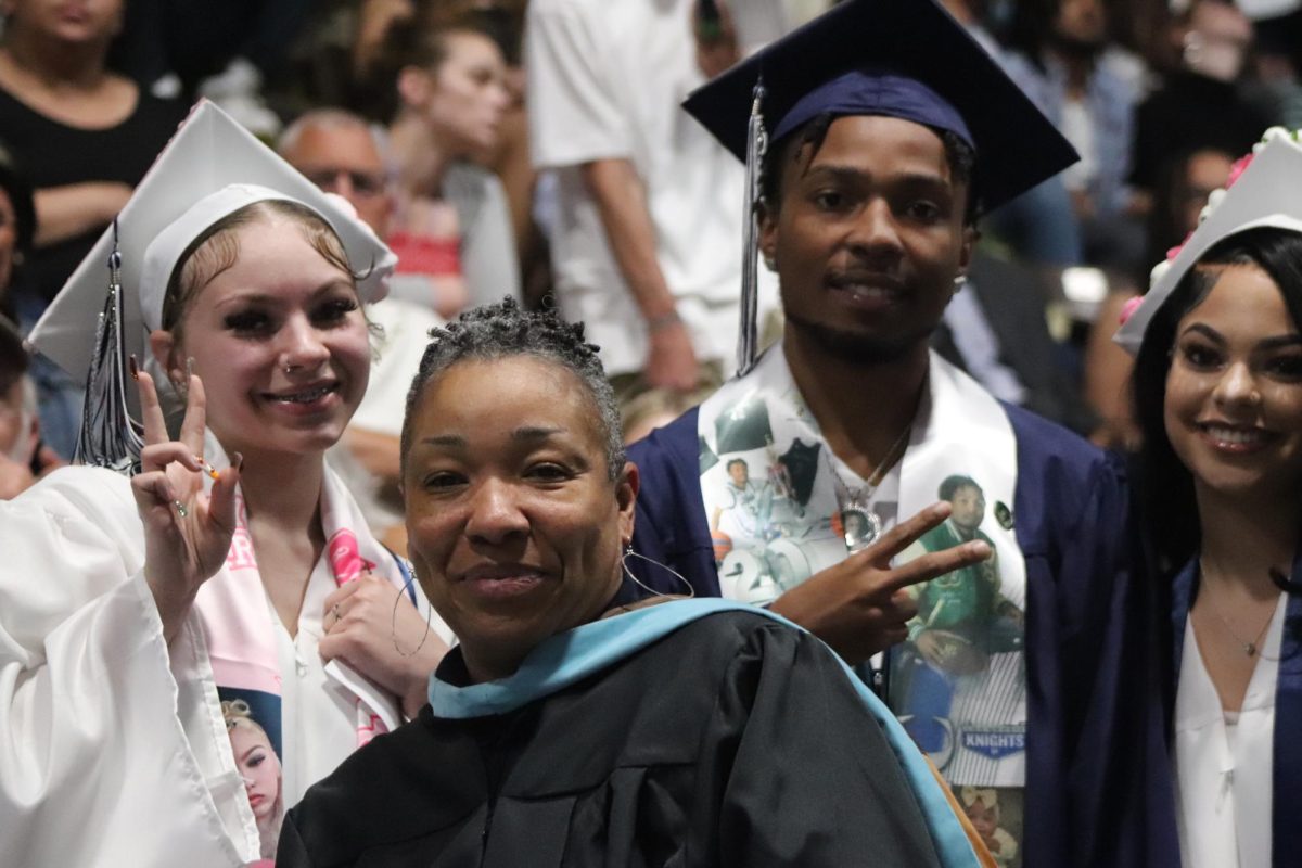 Graduates Imani Hobson, Cedric Huntley, and Emma Mae pose with social studies teacher Niambi McMillon while waiting in line to walk onto the stage.