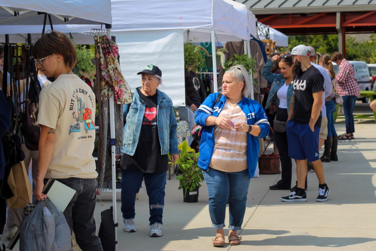 People walking down the aisles of the Kalamazoo Farmers Market, browsing through the different vendors and products.

