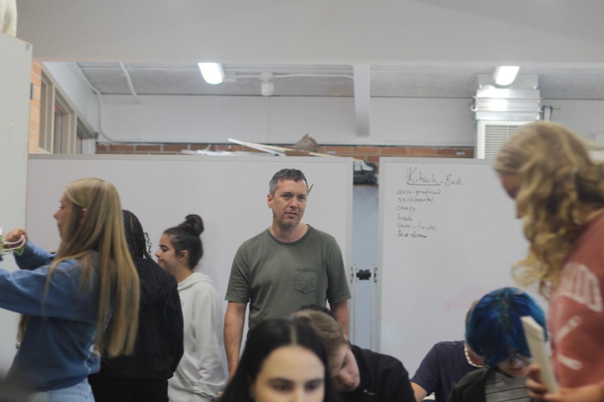 Teacher Gregory Stevens stands in his classroom during his Eco Art class. Students rush to gather materials from one of the classroom cupboards to use in their artwork.
