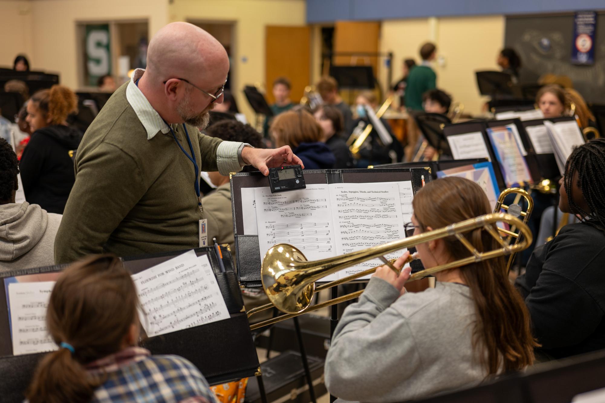 Aaron Mirakovits helps junior Emma Smith tune her trombone in band class. Other students in the class get ready to practice.