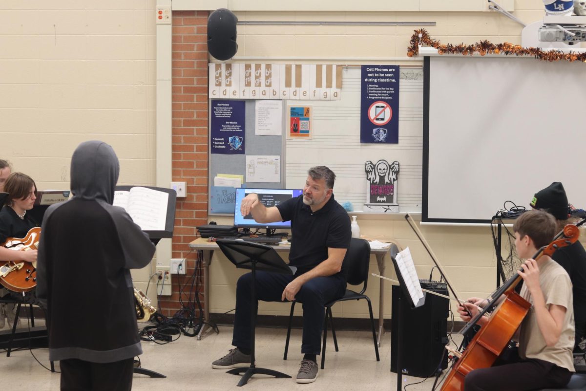 Jazz band director Dennis Shebukhov guides the jazz band through a musical set. The jazz band plays on as Shebukhov makes callouts and shouts measure numbers. 