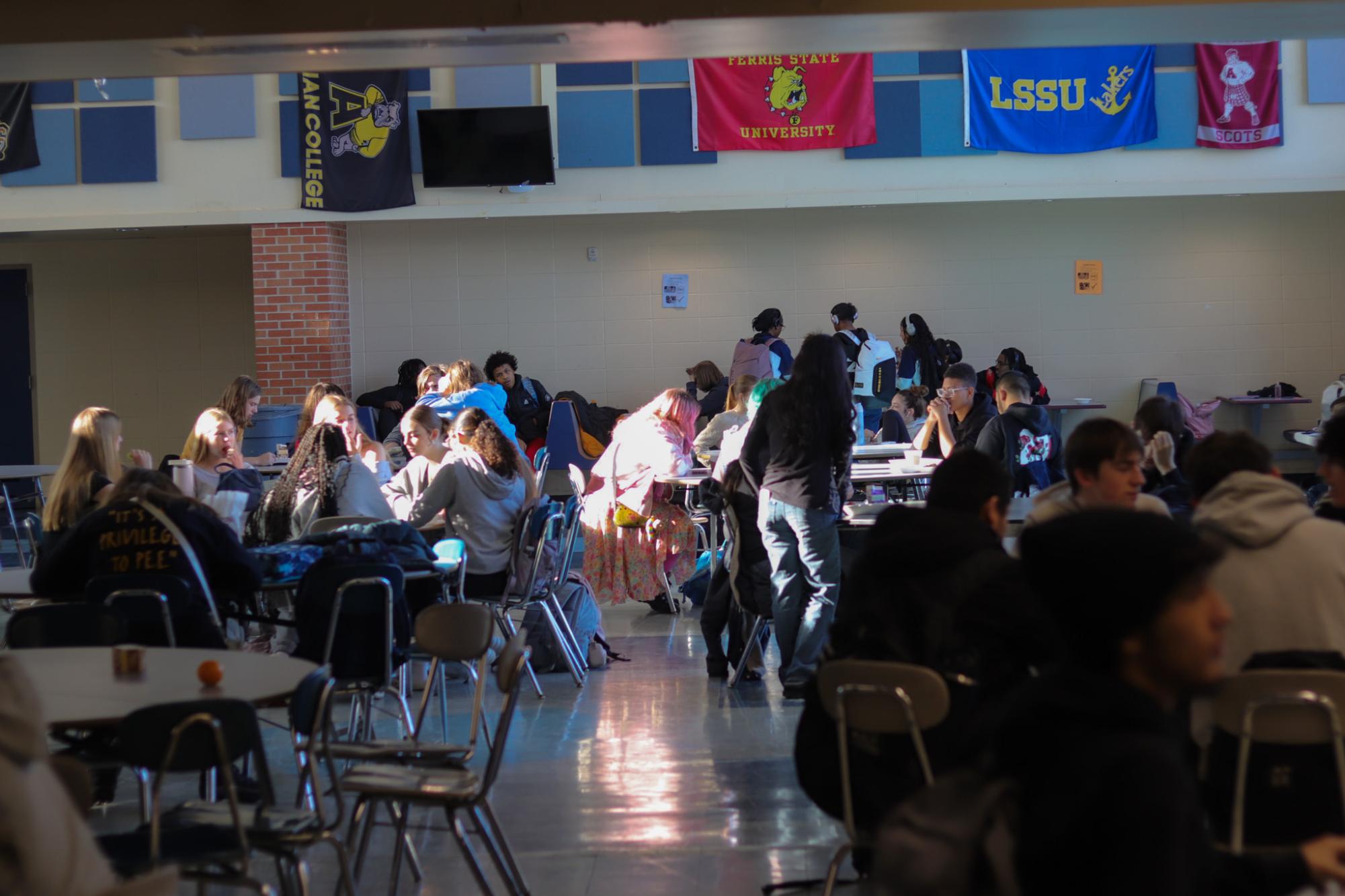 Students mingle during lunch, the sun shining through the windows. The center student, Freshman Rosie Goldstein, is chatting with her friends at their table. 